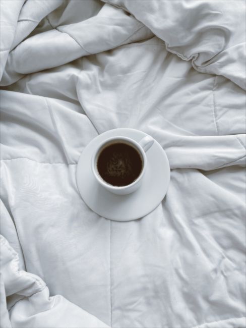 A cup of coffee on a white duvet, evoking a sense of cozy mornings and relaxation.
