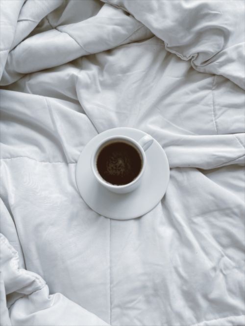 Free A cup of coffee on a white duvet, evoking a sense of cozy mornings and relaxation. Stock Photo