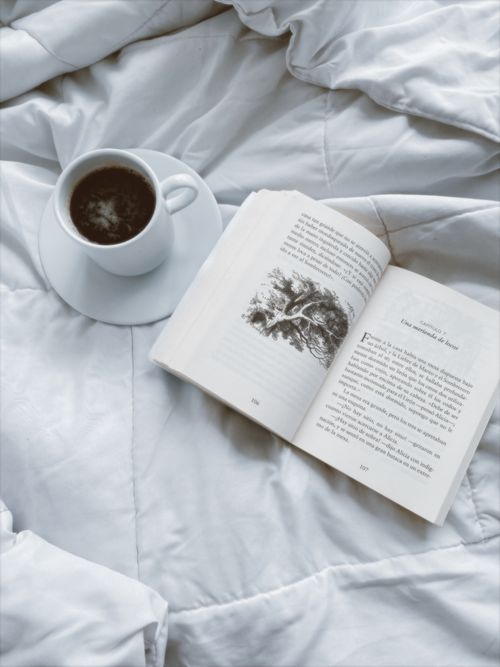Free A cozy setting featuring coffee on a saucer next to an open book on a plush blanket. Stock Photo