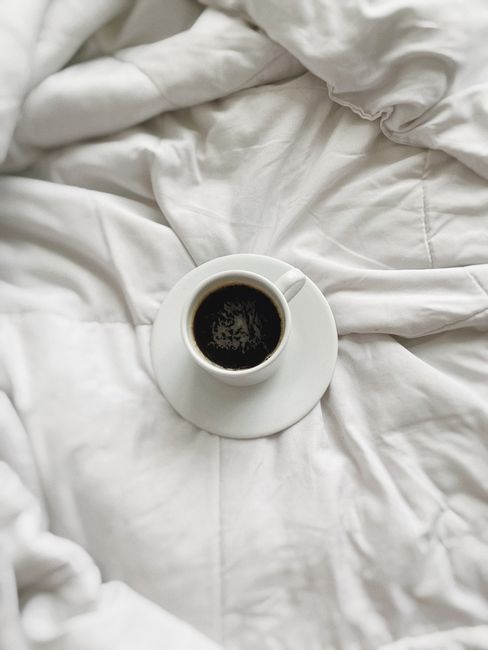 A serene cup of black coffee resting on white bedding. Perfect for mornings.
