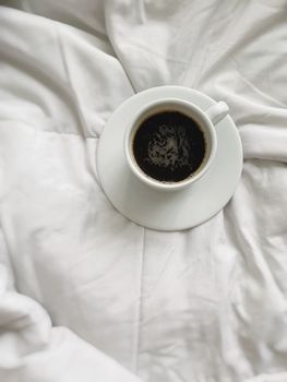 A cozy cup of black coffee placed on a white duvet, offering a warm and inviting vibe.