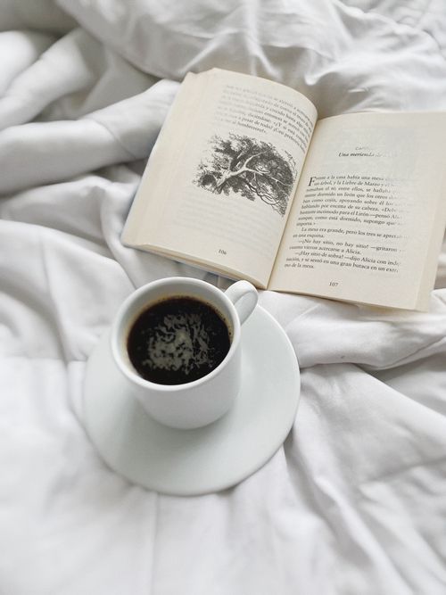 Free A relaxing morning scene with a cup of coffee and an open book on a white bed. Stock Photo