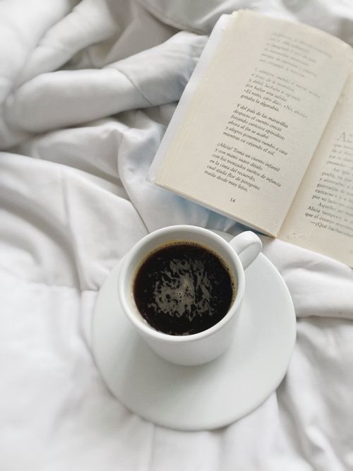 Free Steaming coffee cup and an open book on a cozy white blanket, perfect for relaxed mornings. Stock Photo