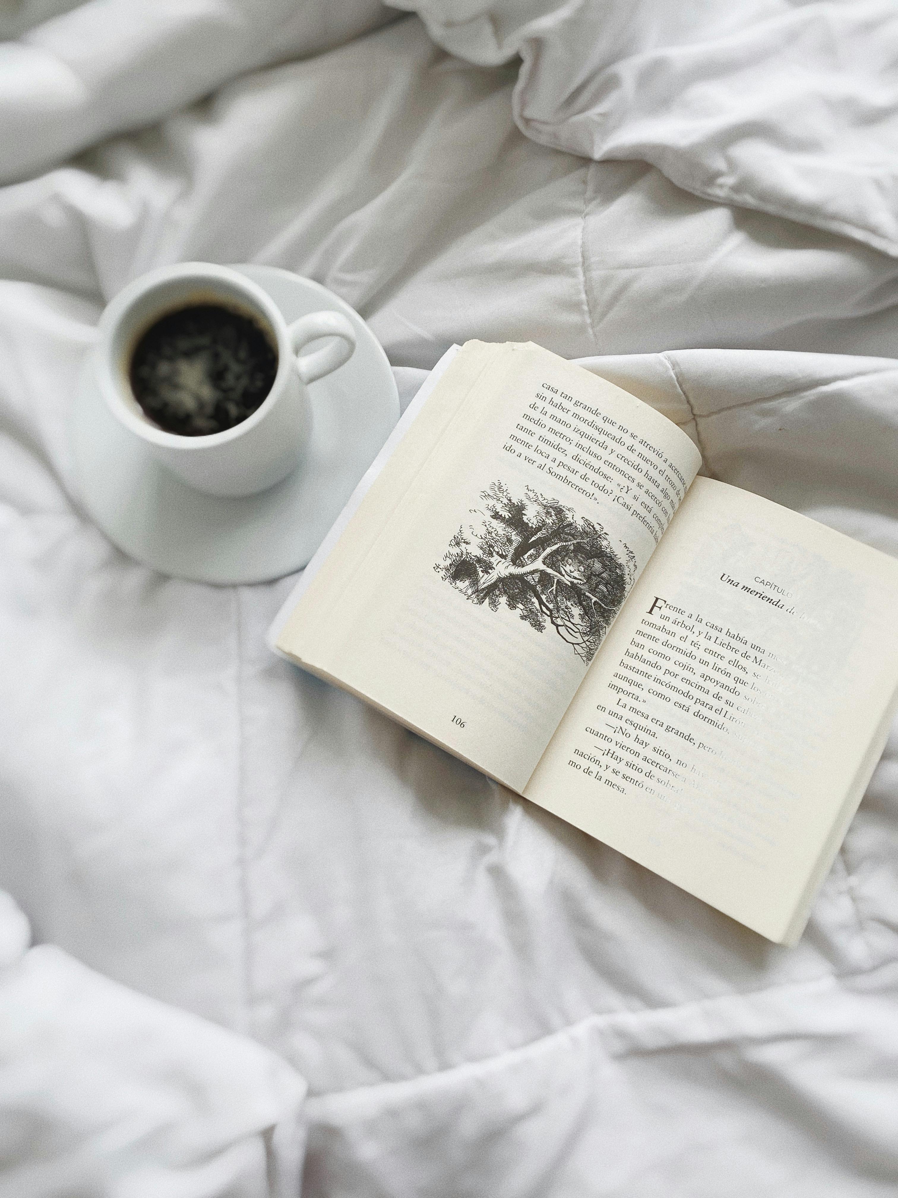 Cozy scene with an open book and coffee cup on a bed, perfect for relaxation.