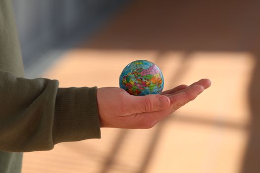 Close-up of a hand holding a small globe with blurred background, emphasizing depth and exploration. 7532231