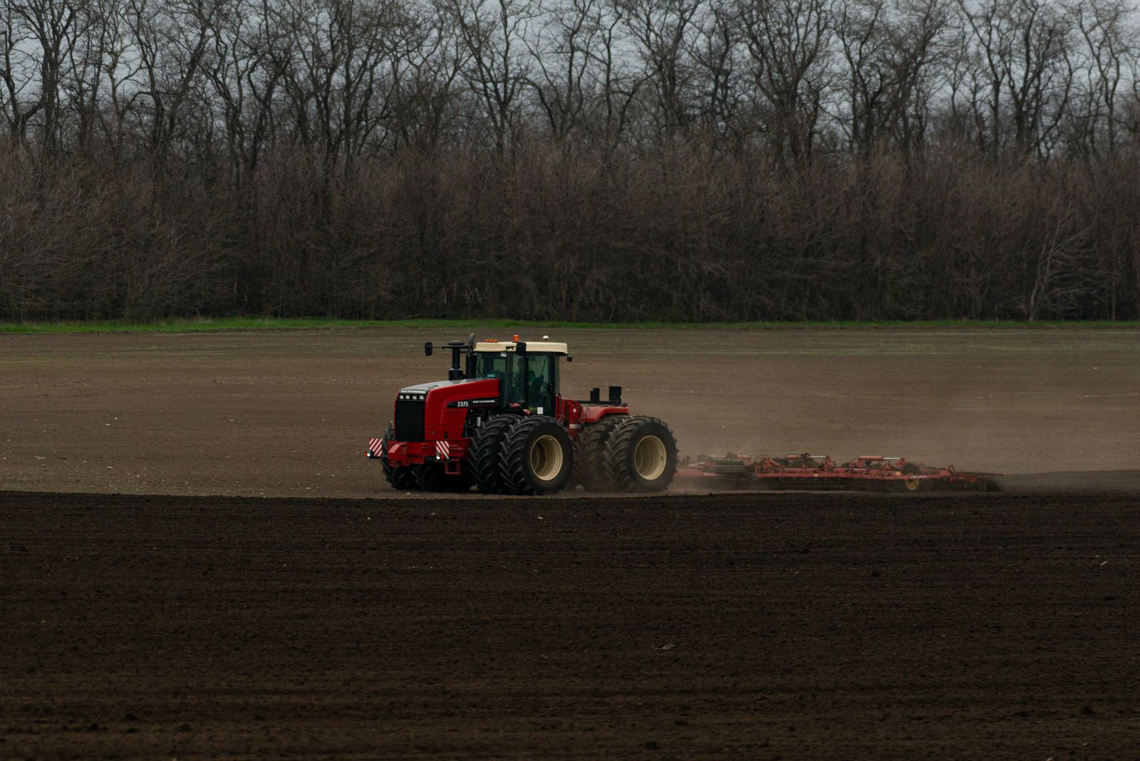 Red tractor tilling a vast field at planting season