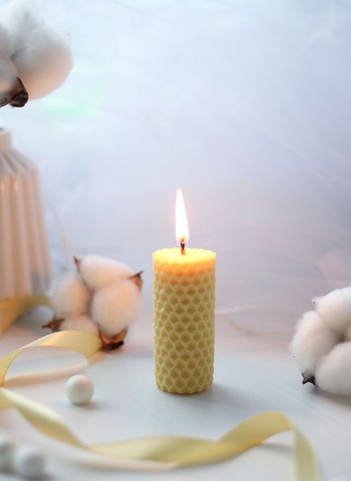 Free A warm yellow candle burns on a table surrounded by cotton flowers, creating a cozy indoor atmosphere. Stock Photo