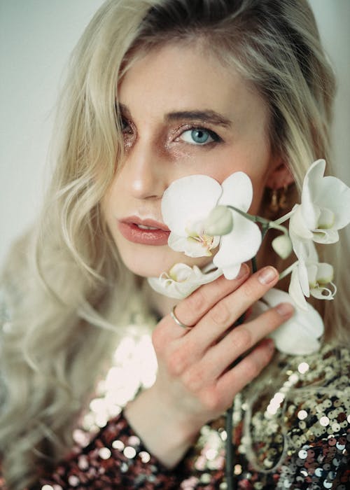 Young woman touching face with blooming orchid