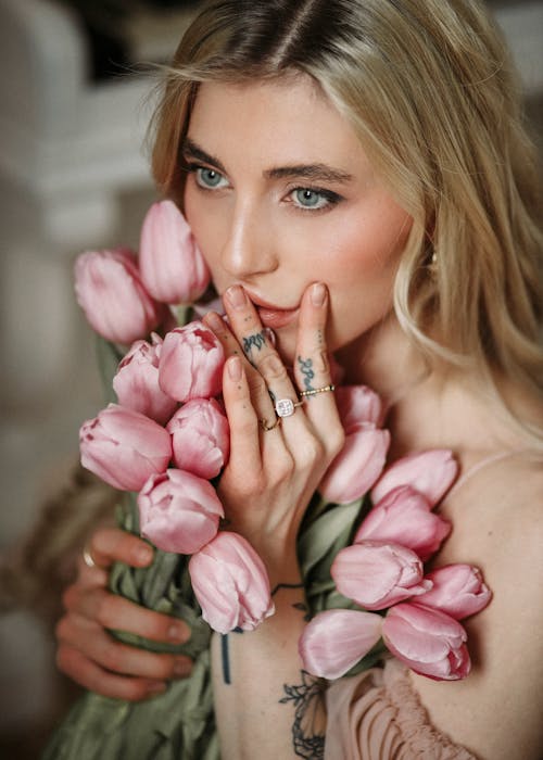 High angle of young female with makeup touching lips and pink blooming tulips and looking away pensively