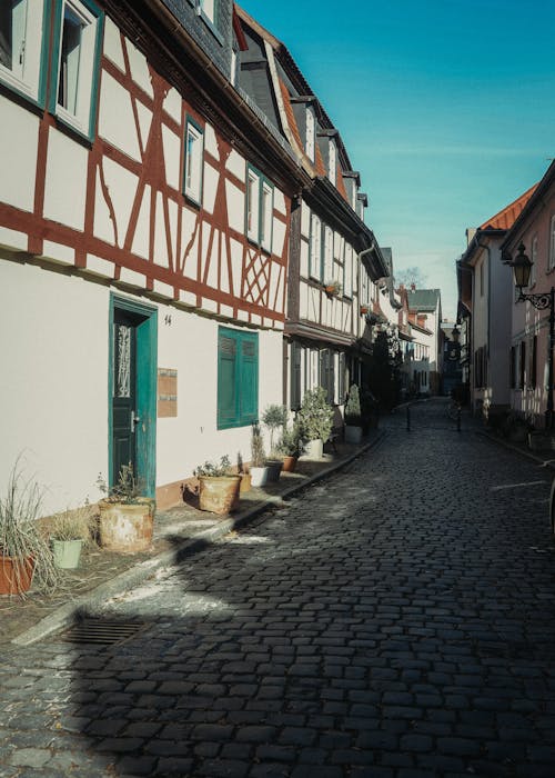 Empty cobblestone street between dwelling buildings located in old town district under cloudless blue sky