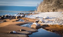 冬日景致静谧，白雪覆盖的海滩、岩石与宁静的溪流相映成趣