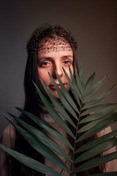 Artistic portrait of a woman partially hidden behind tropical palm leaf in a studio setting.