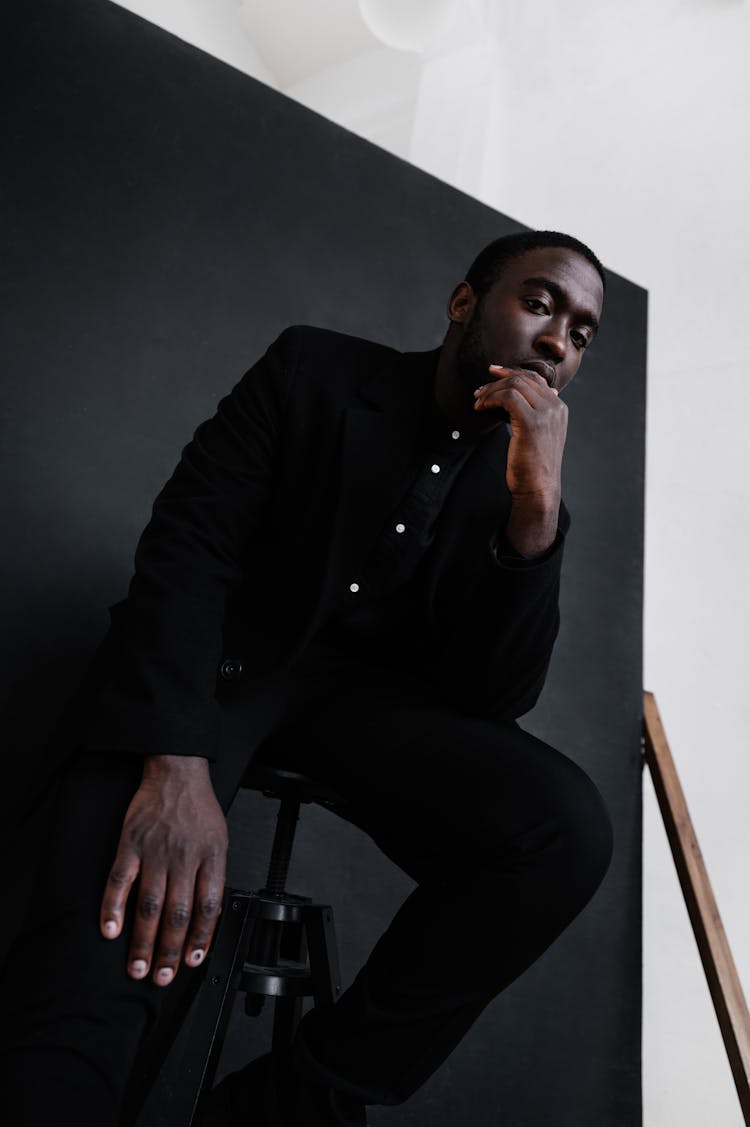 Stylish Black Man Sitting On Chair In Dark Studio