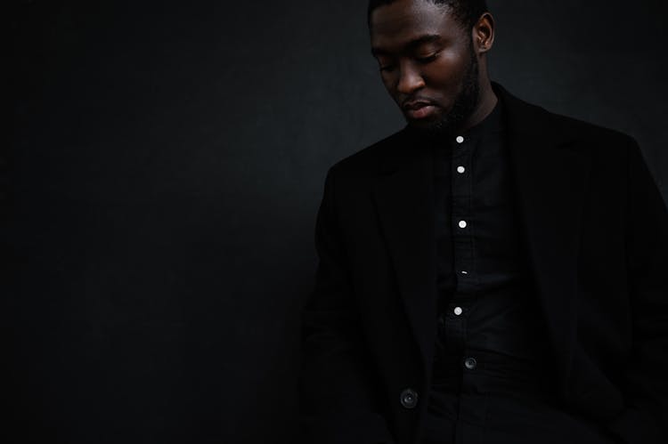 Serious Black Man In Black Suit Standing In Studio