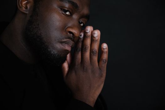 Crop serious African American male with hands together on black background while looking at camera