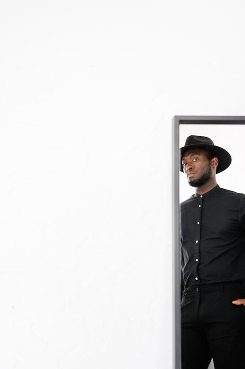 Stylish black man in black suit standing against white wall