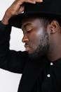 Stylish black man in black suit and hat looking down
