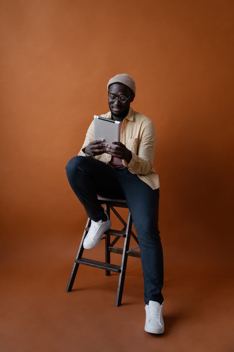 Stylish Black Man Sitting On Chair And Using Tablet