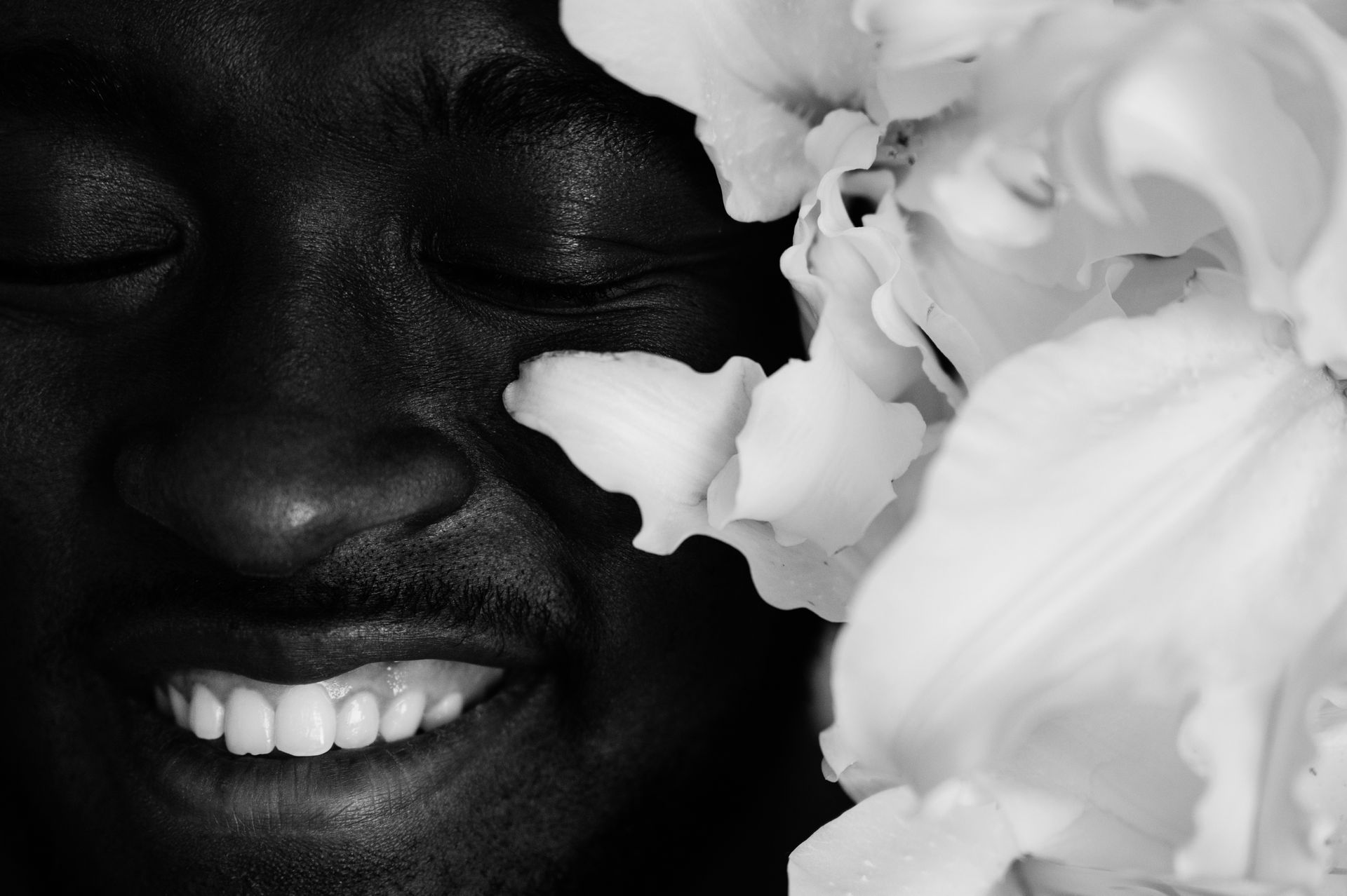 Black and white closeup of African American male with sincere smile and bunch of lily flowers near face