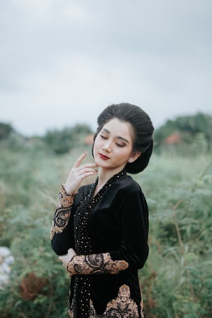 A woman in traditional Asian clothing poses gracefully outdoors with eyes closed and long black hair.