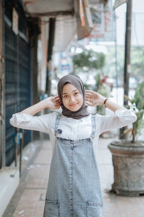 Free A young woman wearing a hijab smiles confidently while standing on a bustling city street. Stock Photo