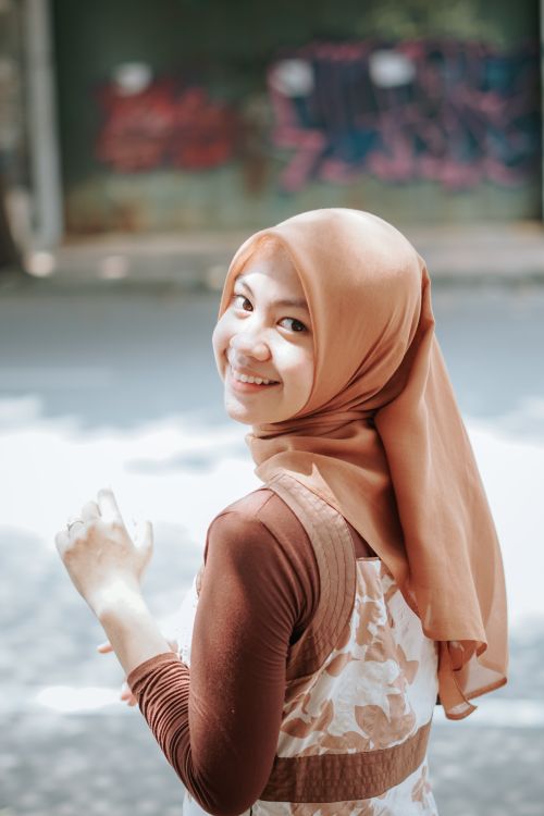 Free A smiling young woman wearing a hijab poses joyfully on a bright sunny street, offering a sense of warmth and positivity. Stock Photo