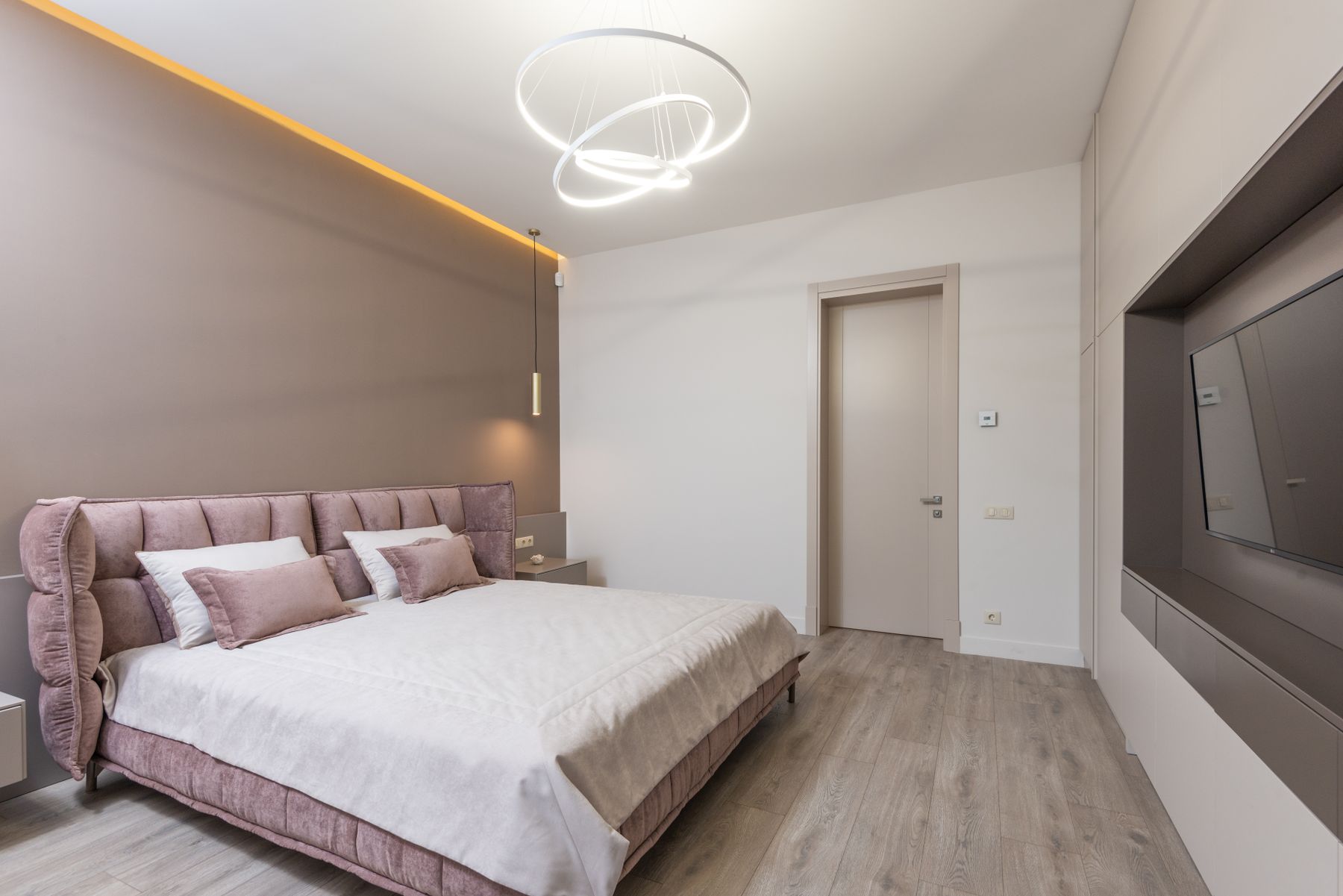 Bedroom with a blush upholstered bed and pillows against warm gray walls, with pale bedding and sculptural ceiling lights