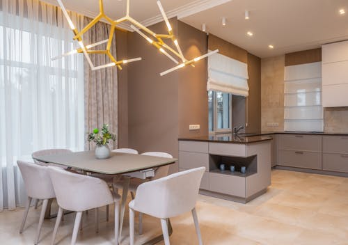 Contemporary open plan kitchen with gray matte cabinets and dining table under contemporary geometric lamp in spacous apartment