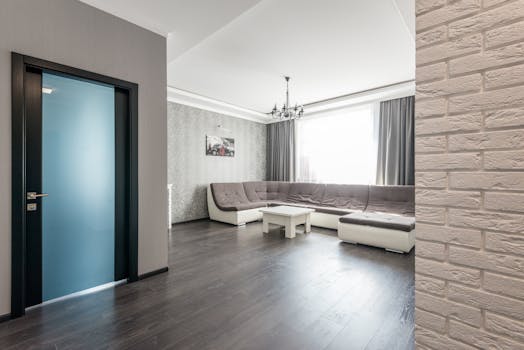 View of empty spacious living room with wooden floor and big comfortable sofa with beige seats and white coffee table near and picture hanging on wall