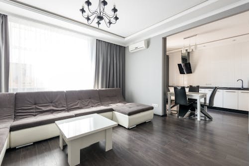 Interior of modern white flat furnished with comfortable couch and dining zone with wooden floor and white walls