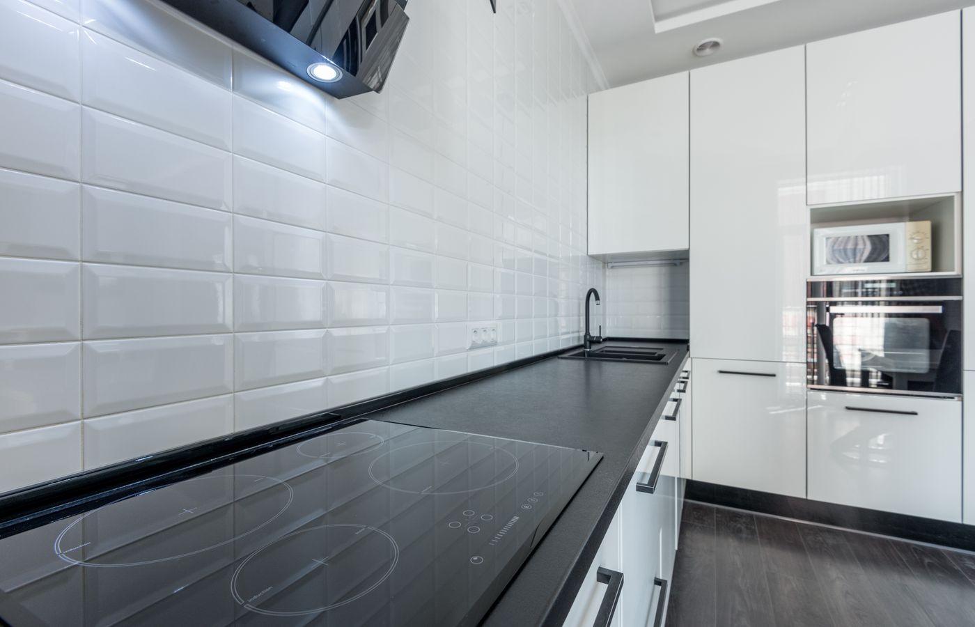 White cabinets and wall tile above a continuous black worktop with sink and cooktop