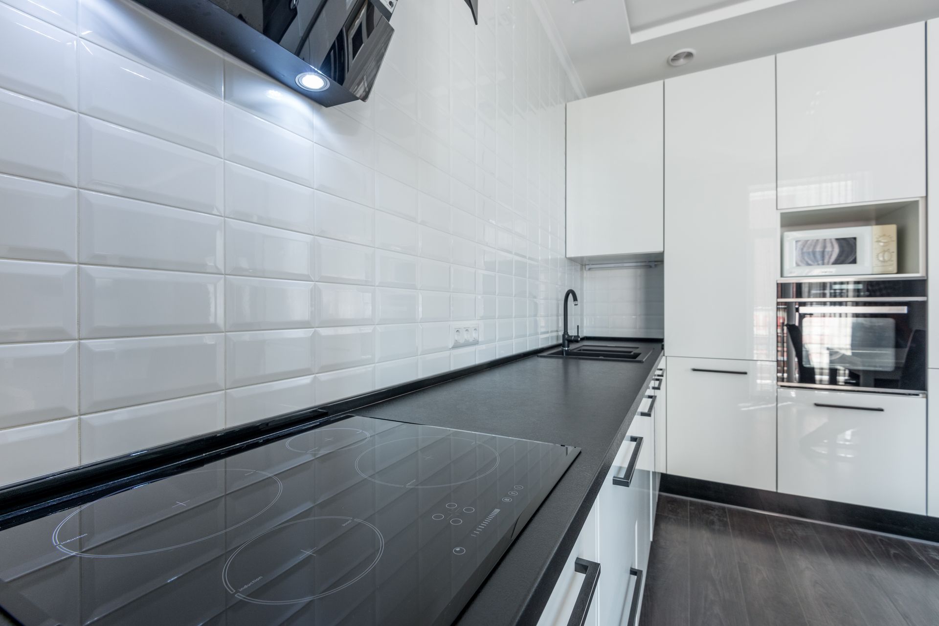 Interior of modern light white kitchen furnished with white cupboards and appliances with wooden floor and tiled wall
