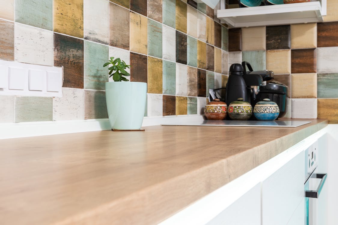 Interior of light kitchen furnished with wooden counter with multicolored tiled backsplash and various dishware