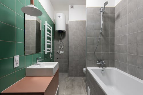 Green and gray tiled walls in contemporary bathroom with white sink and bathtub in minimal style