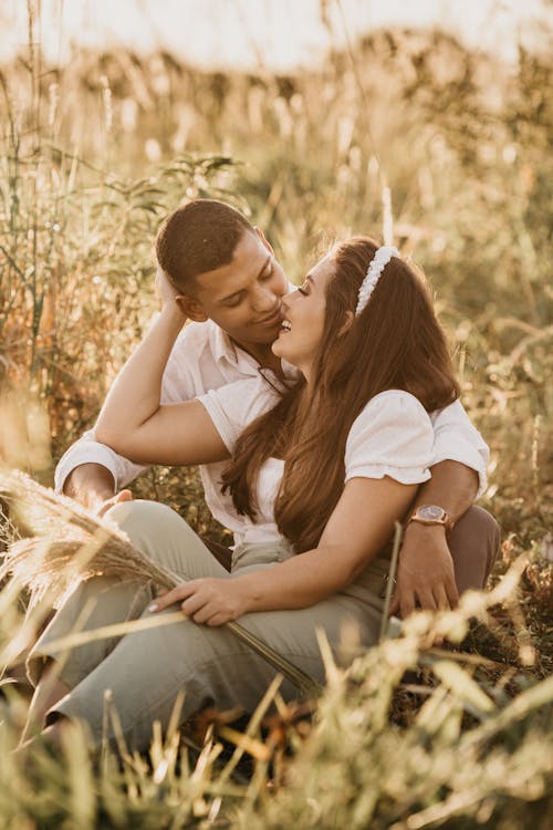 Free Pleasant girlfriend embracing boyfriend while sitting close with bunch of cereal grass in field in countryside Stock Photo