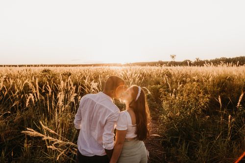 Free High angle back view of romantic couple with closed eyes kissing tenderly in grassy field at sundown in countryside Stock Photo