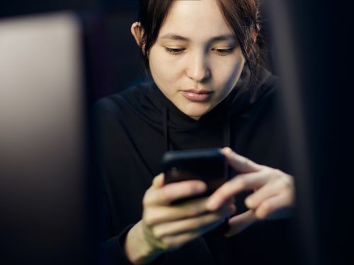 Free A woman intently looking at her smartphone while seated indoors, dim lighting. Stock Photo