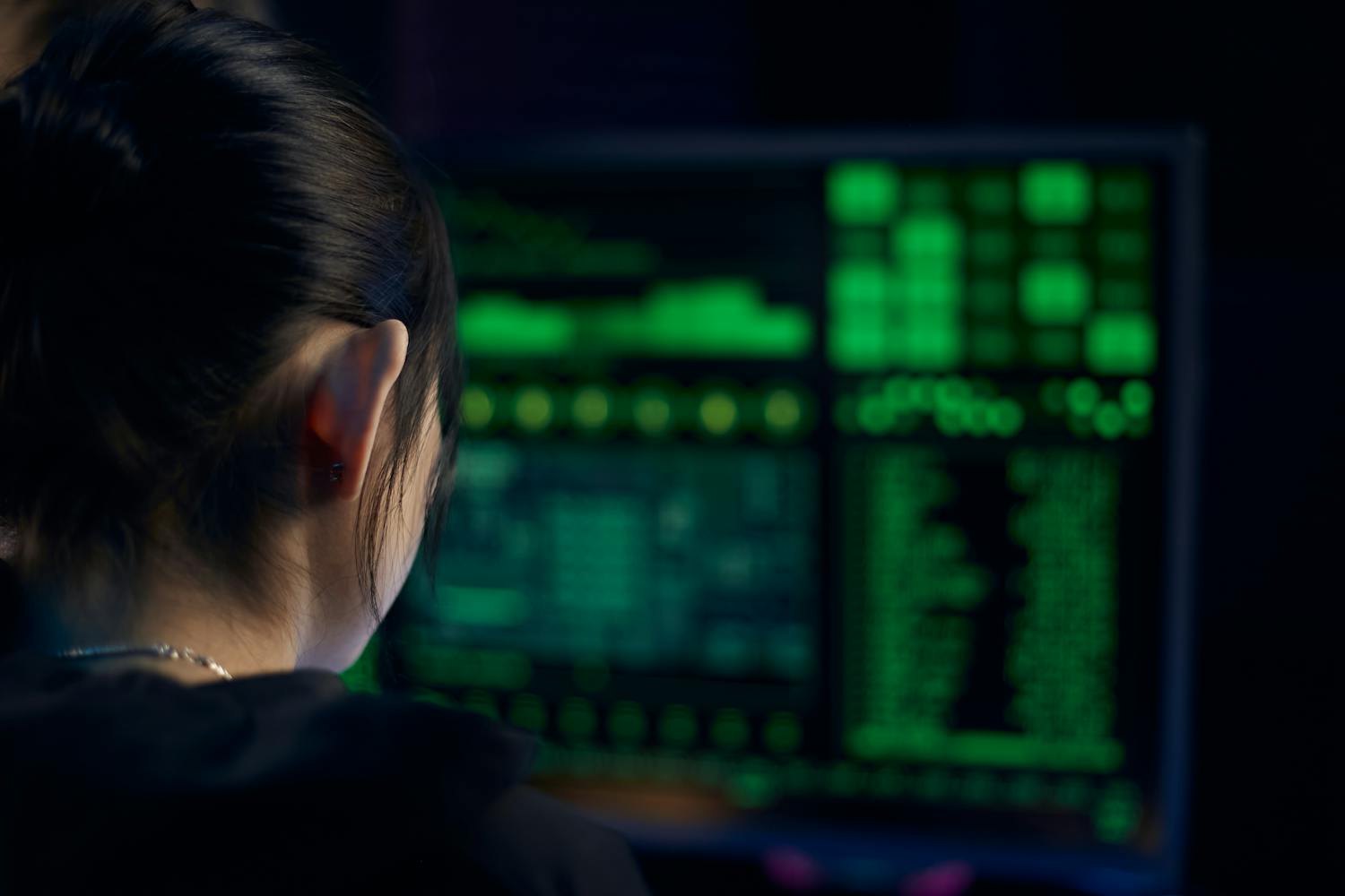 A woman focuses on data displayed on a computer screen in a dark room