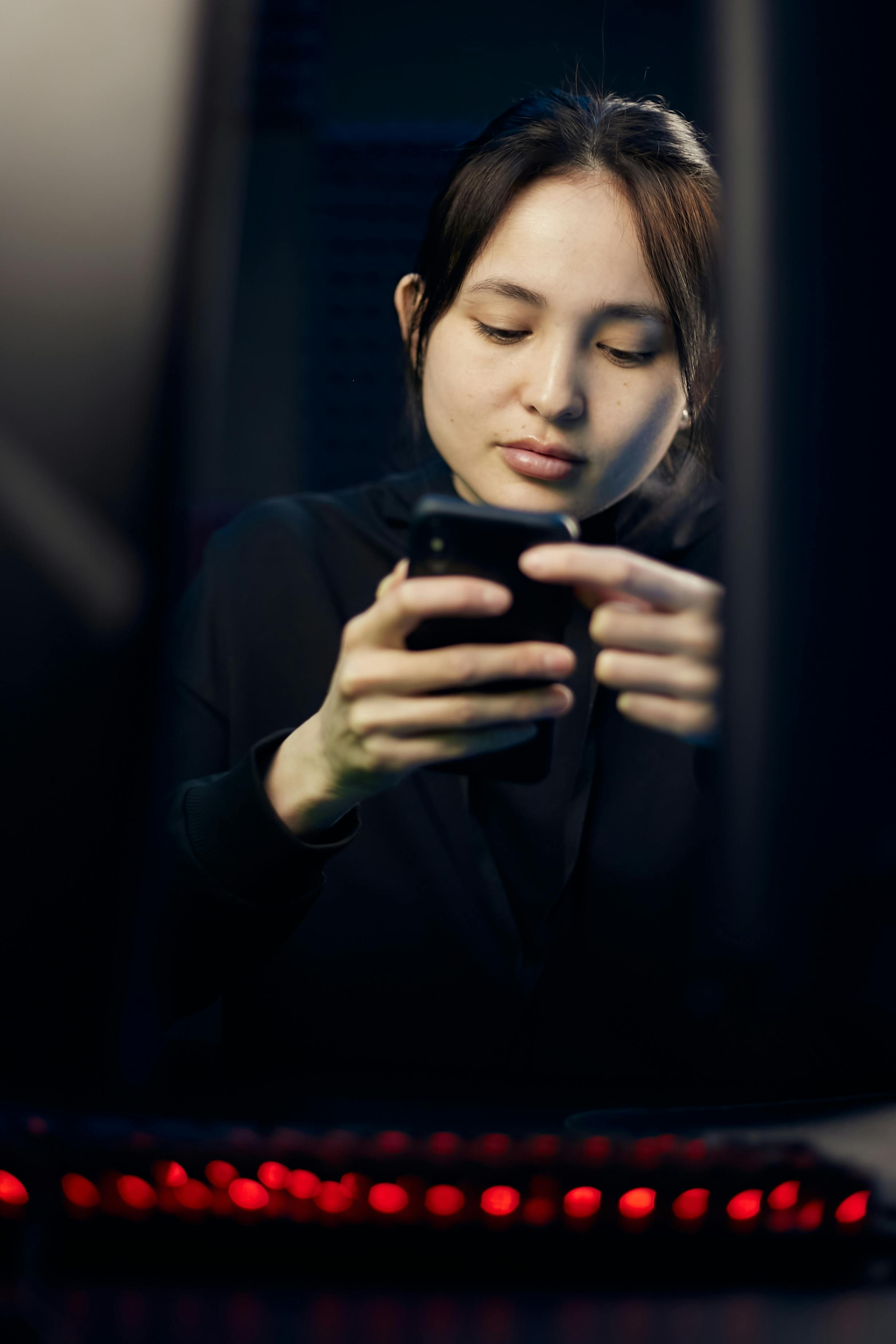 Free A woman in black long sleeves using a smartphone in a dim room with a blurred background. Stock Photo