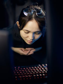 A young woman in a black hoodie focused on a computer keyboard with illuminated keys.