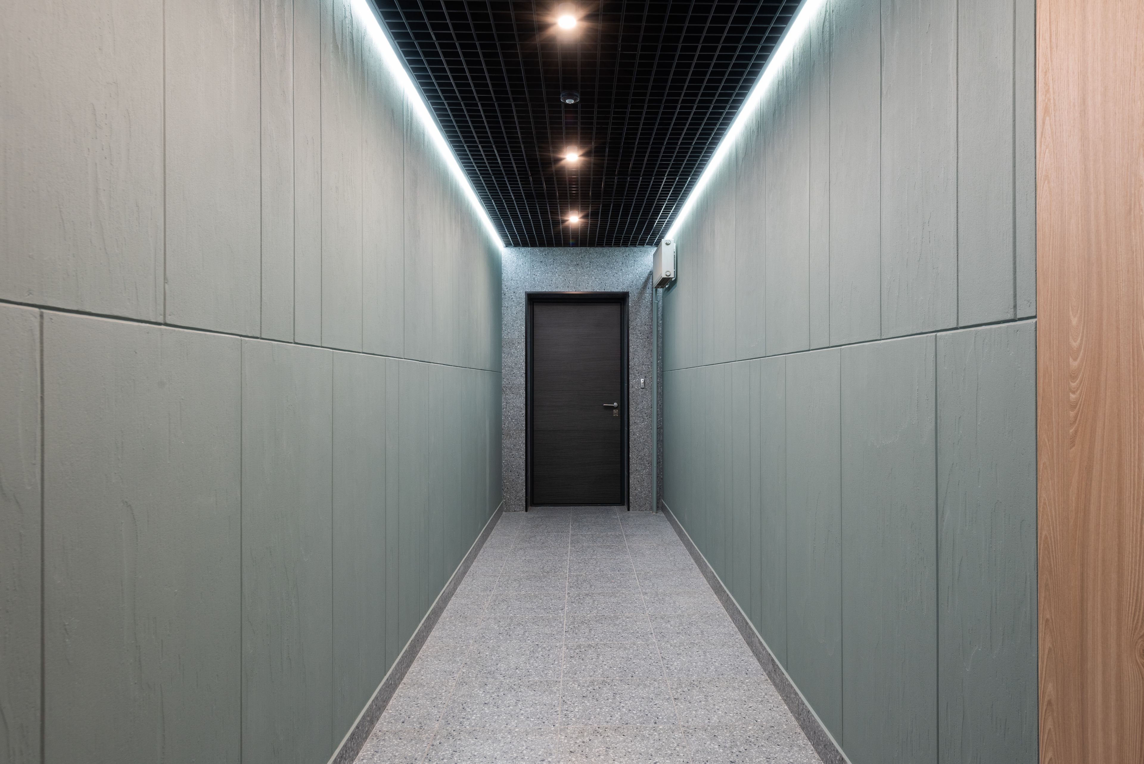 Long couloir vitré d'un immeuble de bureaux contemporain, sol clair et cloisons transparentes