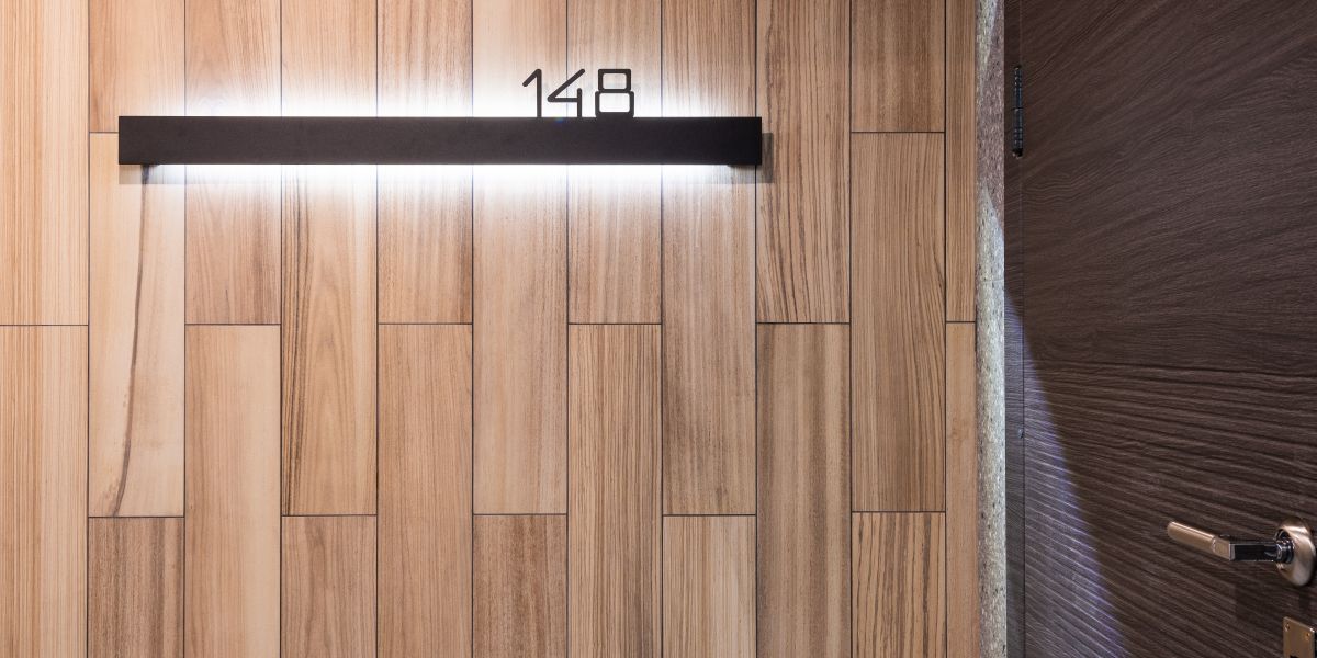 Illuminated room number on a wooden panel wall beside a hotel room door