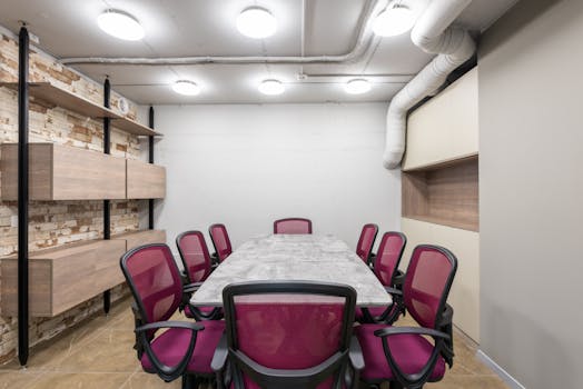 Table and chairs placed in modern conference hall in workspace illuminated by ceiling lamps