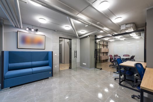Interior of contemporary spacious workspace furnished with comfortable sofa and blue office chairs at tables