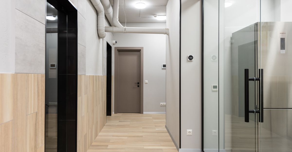 Um corredor de escritório elegante e minimalista com paredes de vidro e piso de madeira.