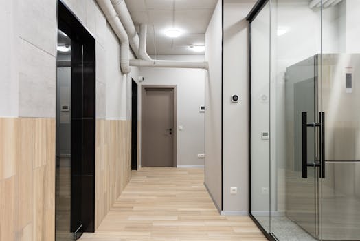 A sleek, minimalistic office hallway featuring glass walls and wooden flooring.