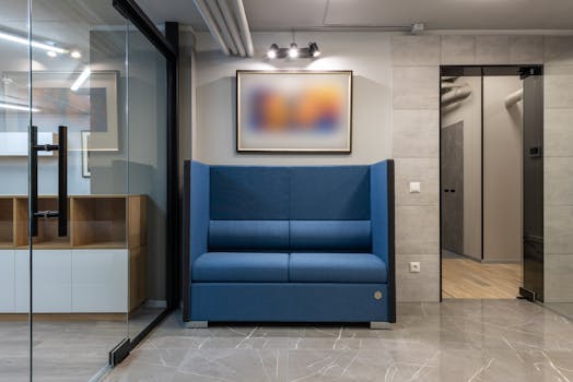 Spacious contemporary office lounge featuring a blue sofa, glass doors, and minimalistic decor.