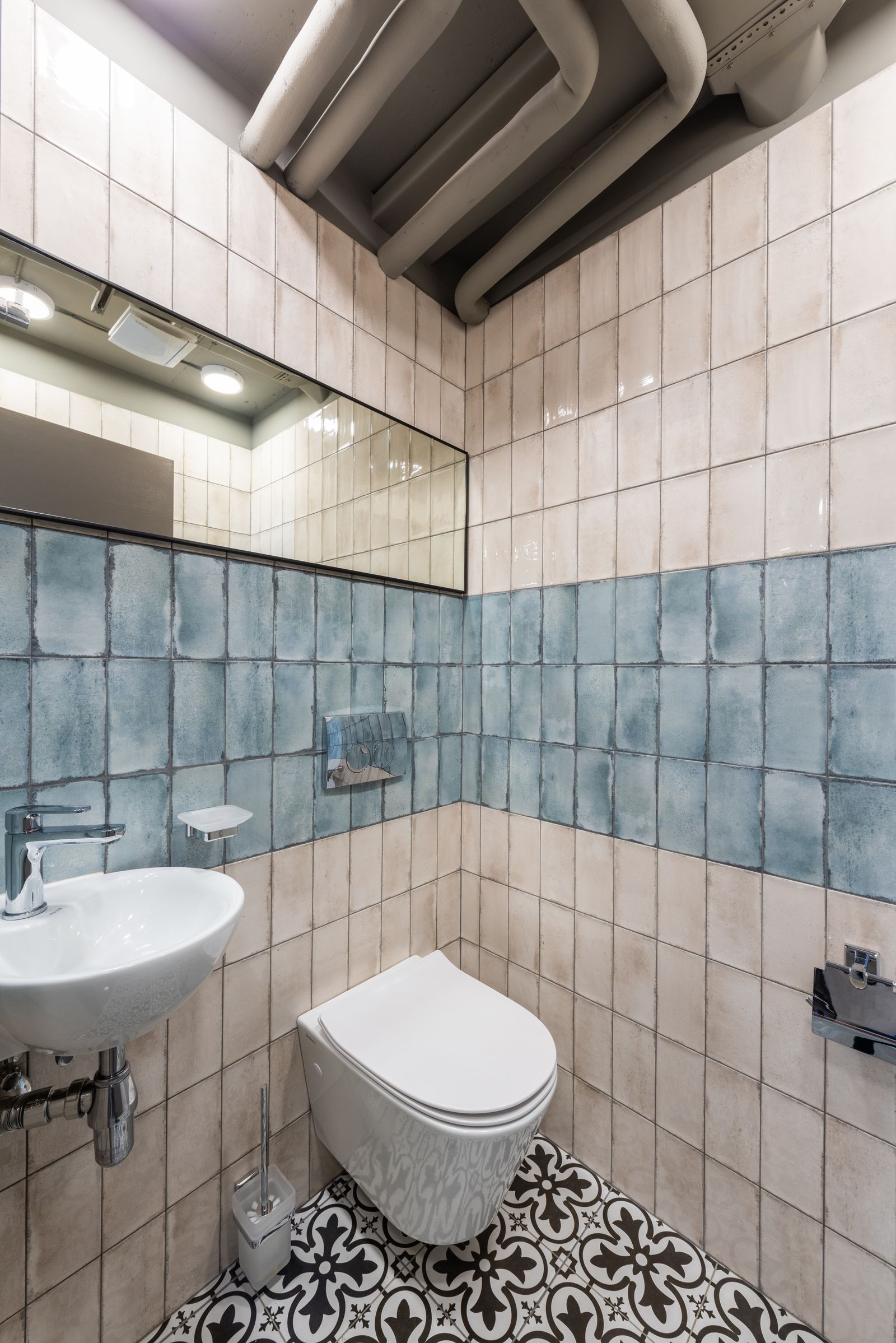 Black-and-white decorative floor tiles in a compact toilet room with blue and cream wall tiles.