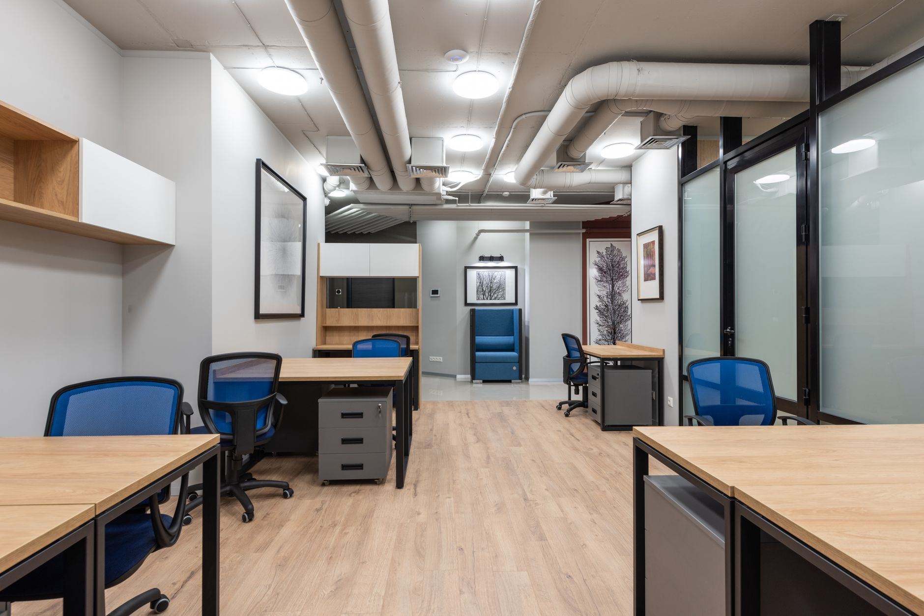 Wooden tables and office chairs placed in modern workplace with bright illumination from ceiling lamps