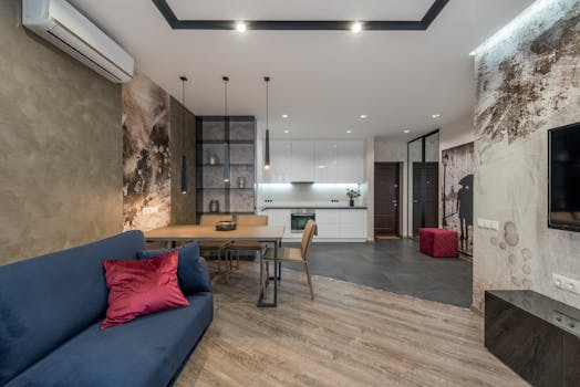 A stylish contemporary living room with modern furnishings and decor, featuring a blue sofa and open kitchen.